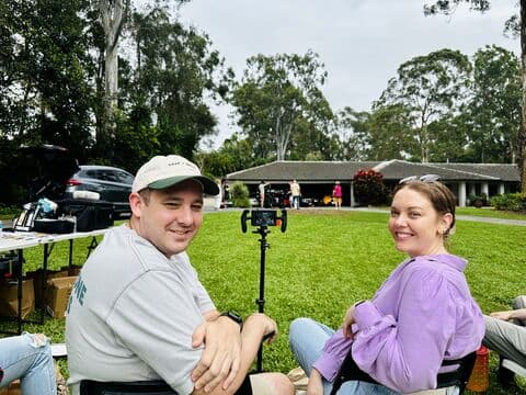 Bec in a purple shirt and Nick Harris, Campaign Coordinator, seated beside filming equipment on the lawn, with Nick looking back towards the camera