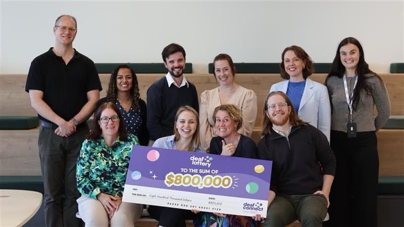 Deaf Lottery team members gathered around a large $800,000 prize cheque carrying the earlier dotted lottery identity